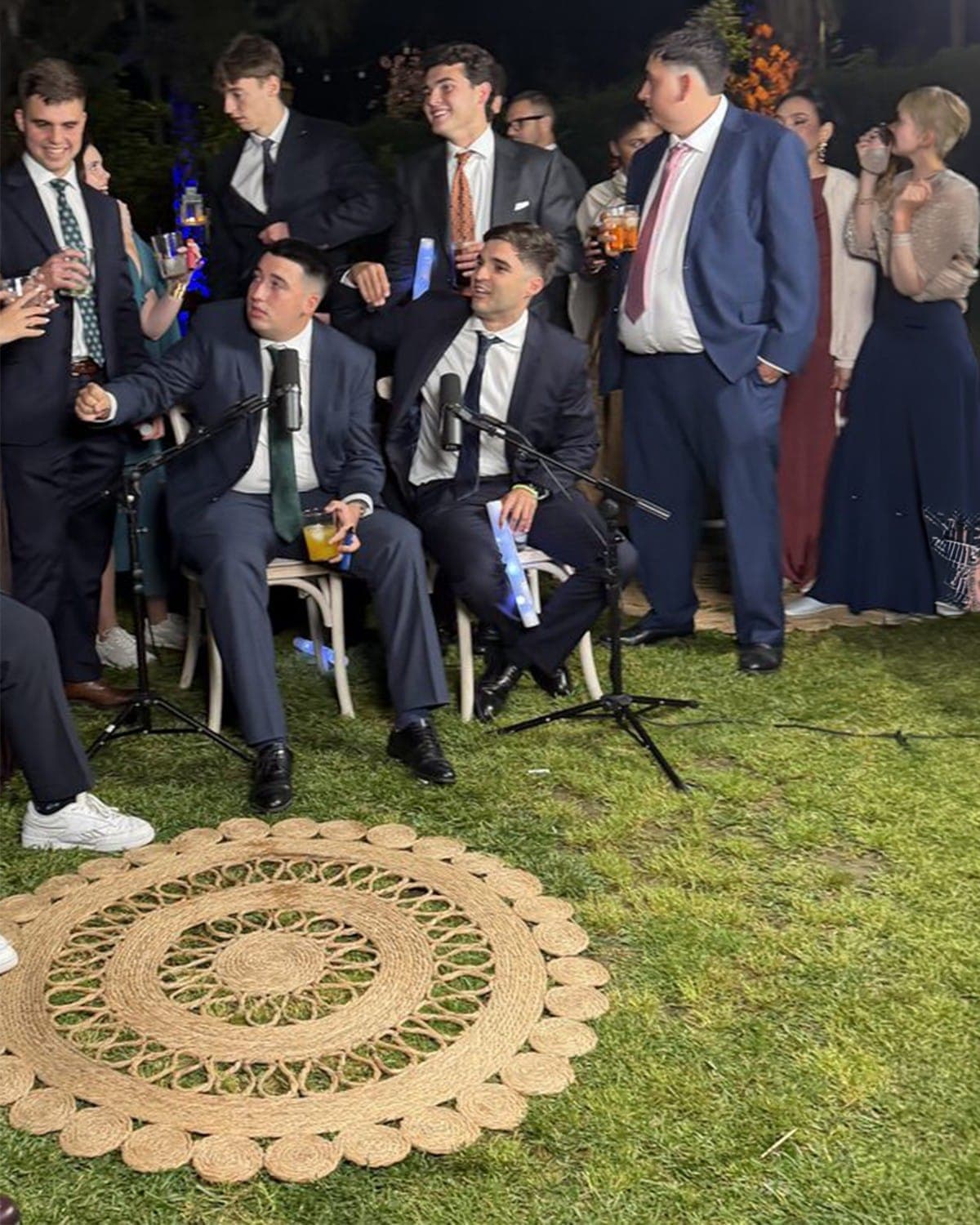 Invitados sentados frente a micrófonos mientras la fiesta sigue alrededor